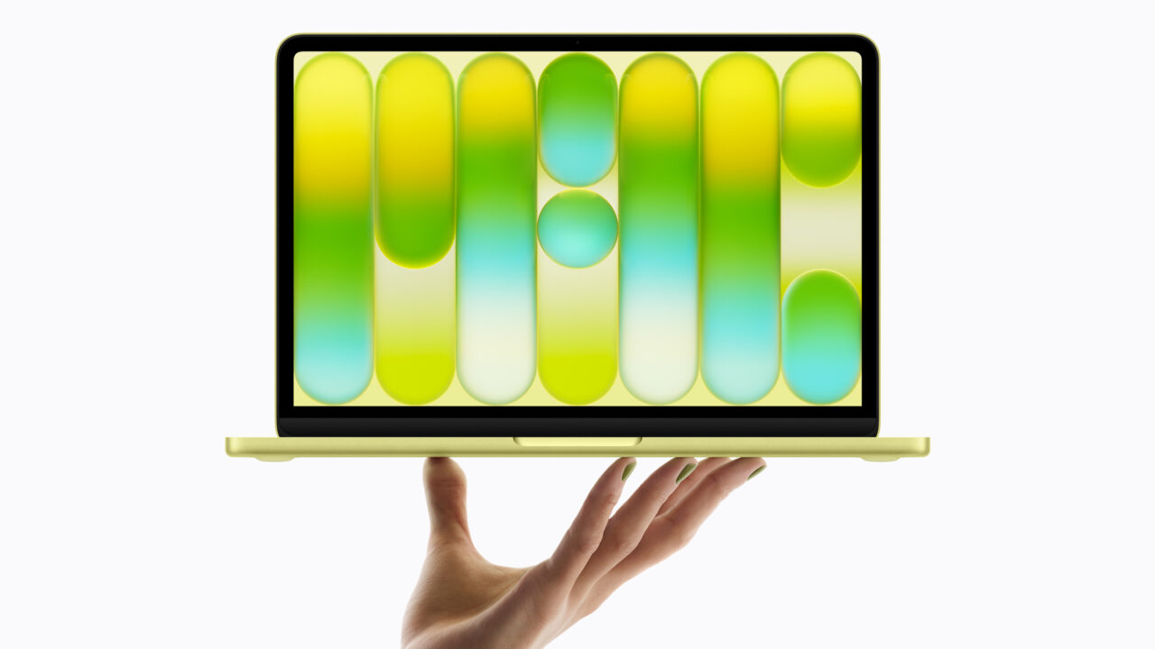 A hand holds up the all-new MacBook Neo in citrus.