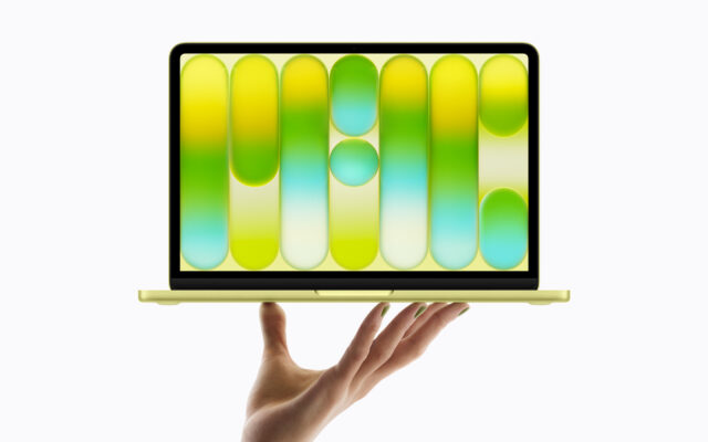 A hand holds up the all-new MacBook Neo in citrus.