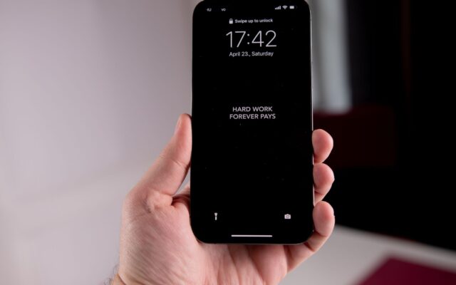 Close-up of a hand holding a smartphone displaying the motivational quote 'Hard Work Forever Pays.'