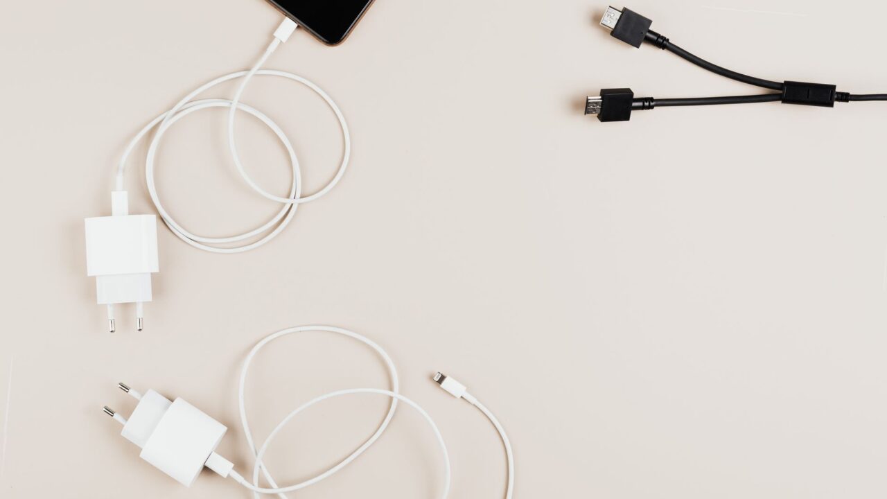 Flat lay of mobile devices with chargers and cables on a neutral background.
