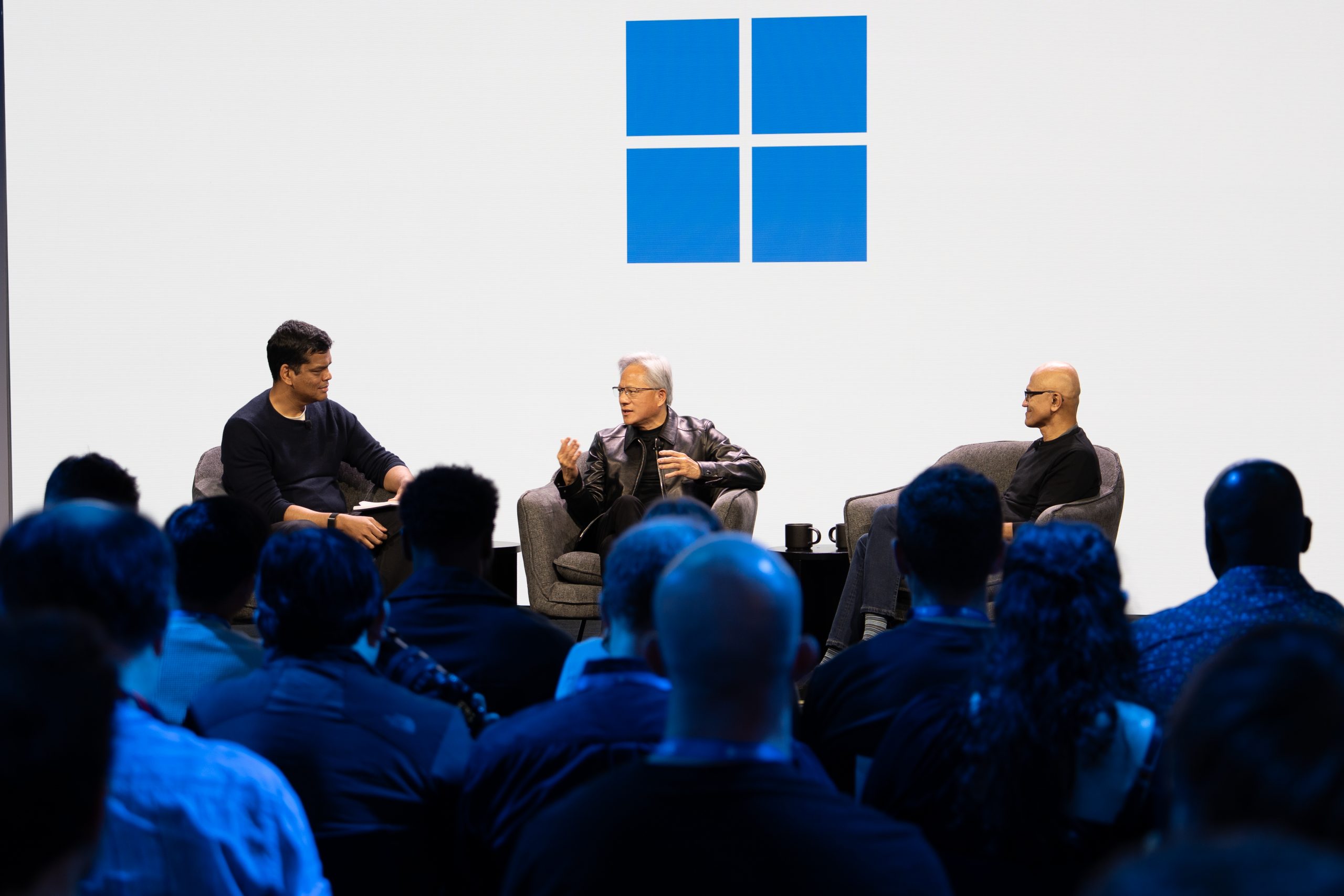 Three men having a conversation on stage below the Windows logo