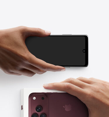 Hands exchanging phones, Android on the left without box, new iPhone 18 Pro, burgundy color (dark red), in box, on the right