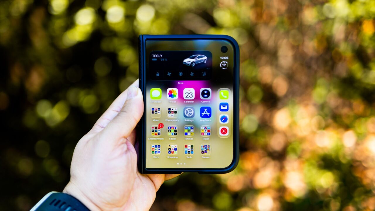 Close-up of a hand holding a foldable smartphone showing apps, outdoors with blurred background.