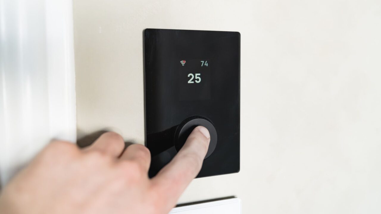 A hand adjusting a modern smart thermostat mounted on a wall
