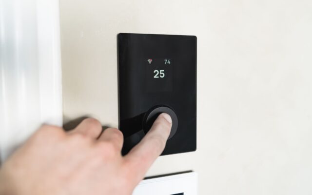 A hand adjusting a modern smart thermostat mounted on a wall
