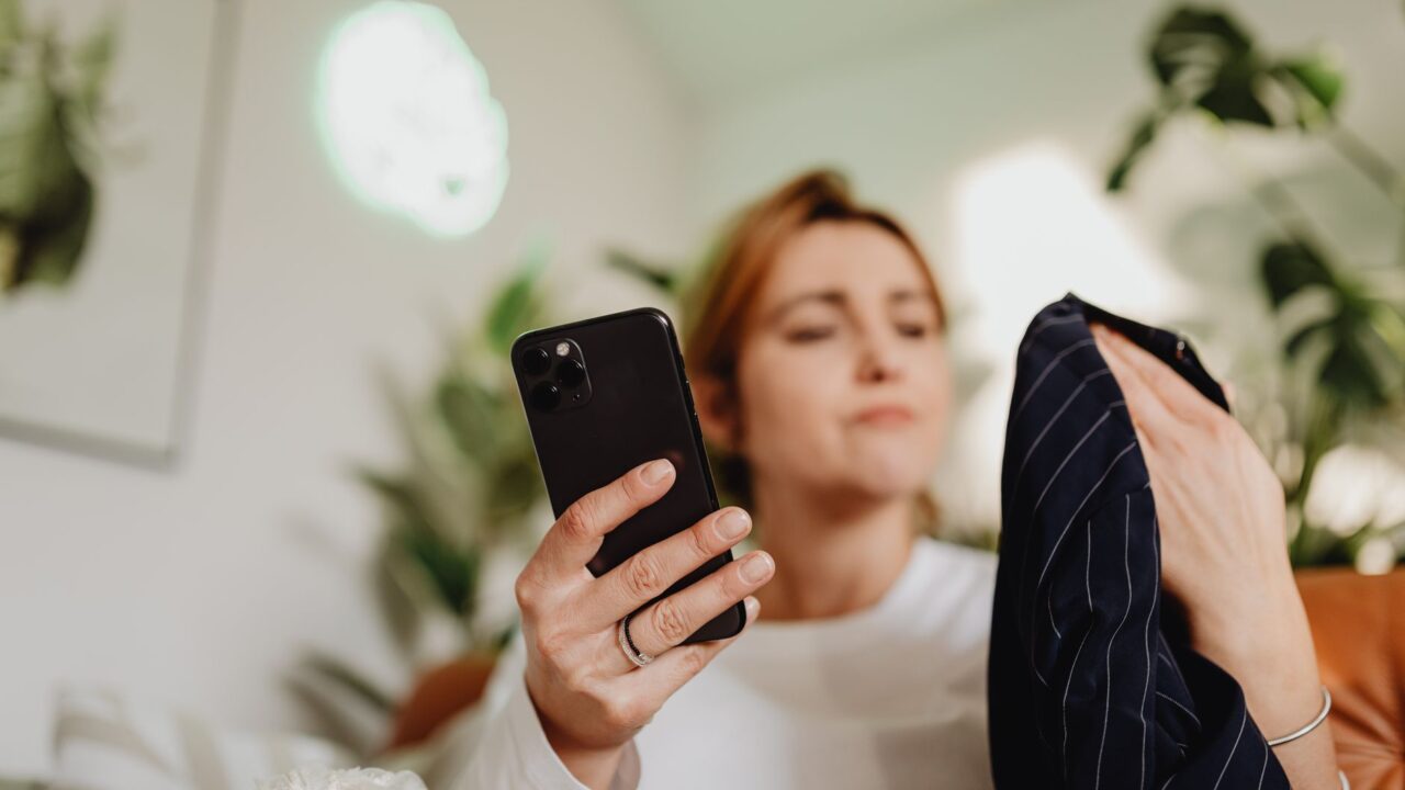 A woman uses her smartphone indoors for online shopping, holding fabric.