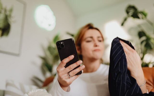 A woman uses her smartphone indoors for online shopping, holding fabric.