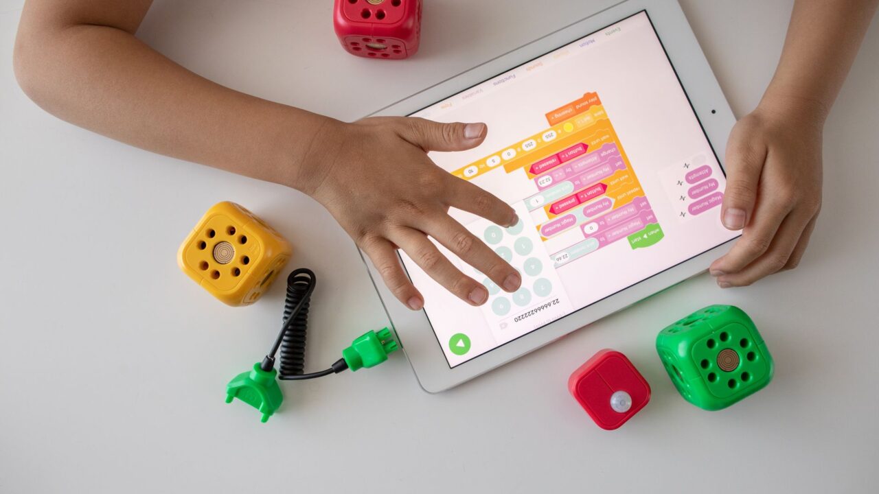Child using digital tablet for coding education alongside colorful toy blocks.