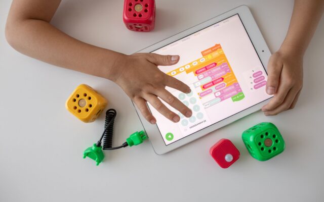 Child using digital tablet for coding education alongside colorful toy blocks.