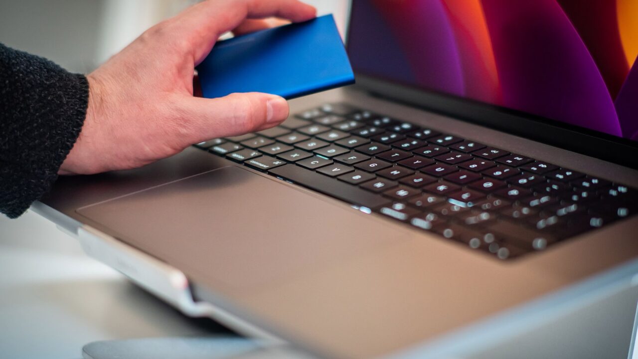 A hand holding a portable drive over a laptop keyboard