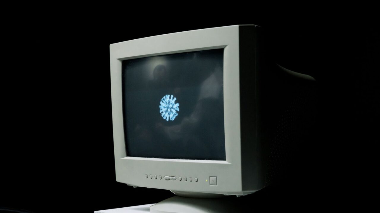A vintage computer monitor shows an image of a coronavirus on screen against a dark background.