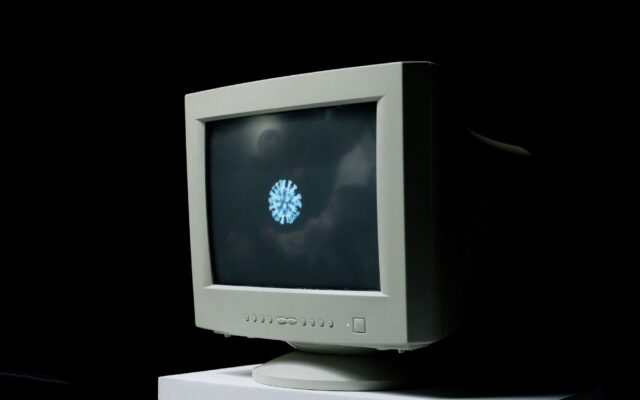 A vintage computer monitor shows an image of a coronavirus on screen against a dark background.
