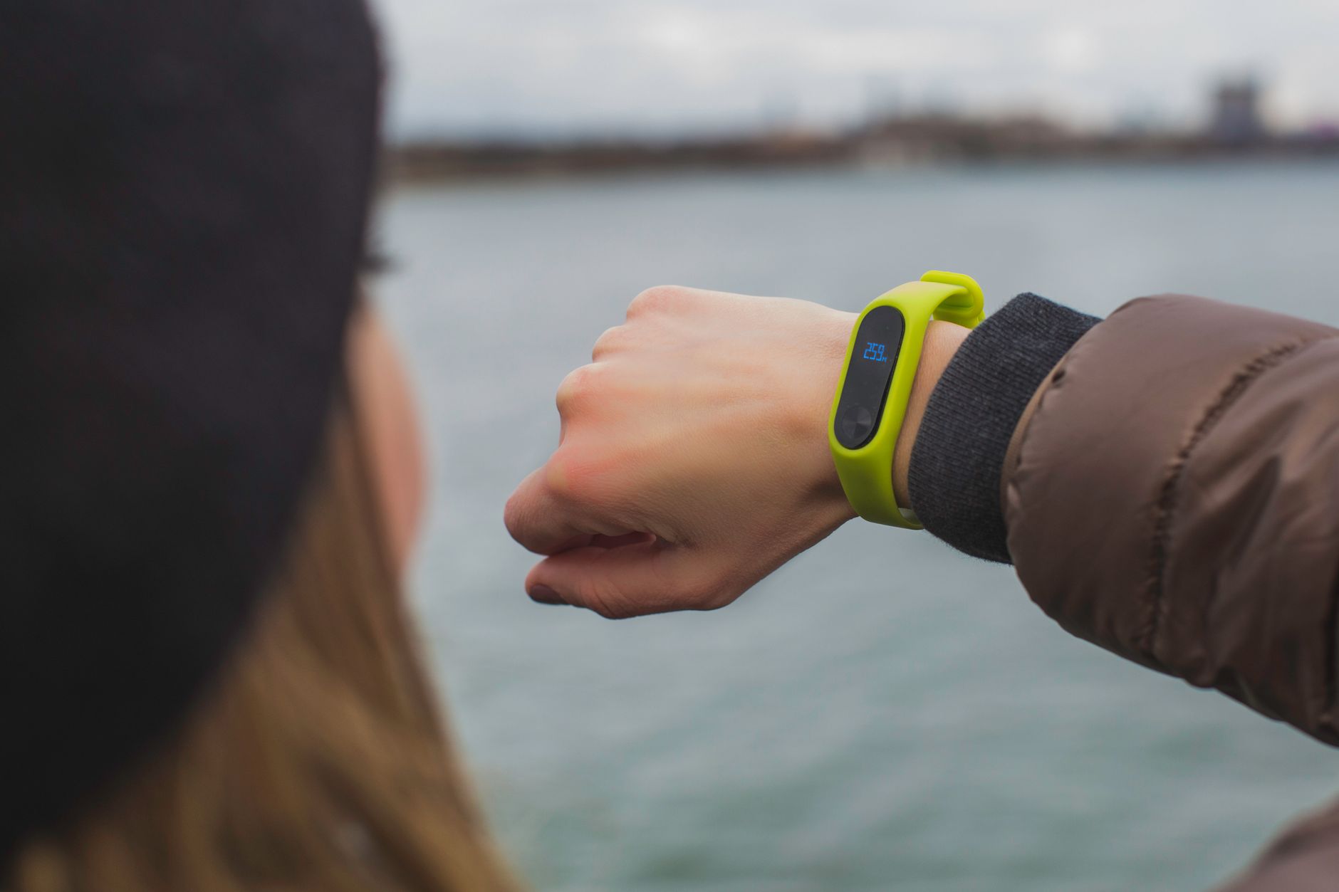 A person checking a fitness band on their wrist by a lake