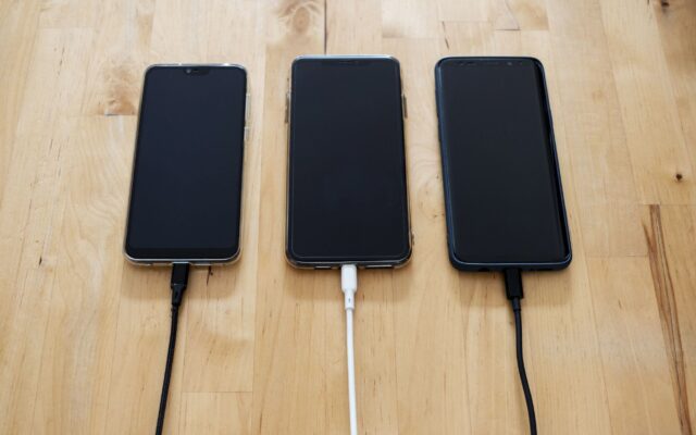 Three smartphones connected to chargers on a wooden surface, showcasing modern technology