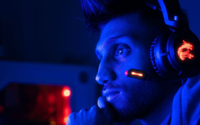 A gamer wearing a headset with a microphone in blue light