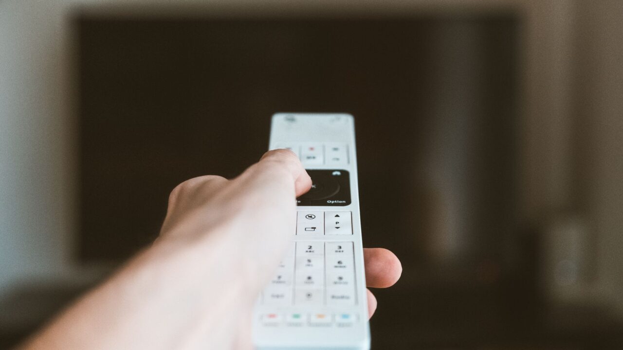 A hand pointing a remote control at a TV