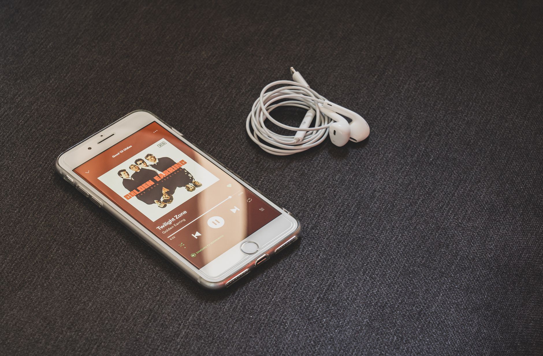 An iPhone playing music next to a pair of wired earbuds