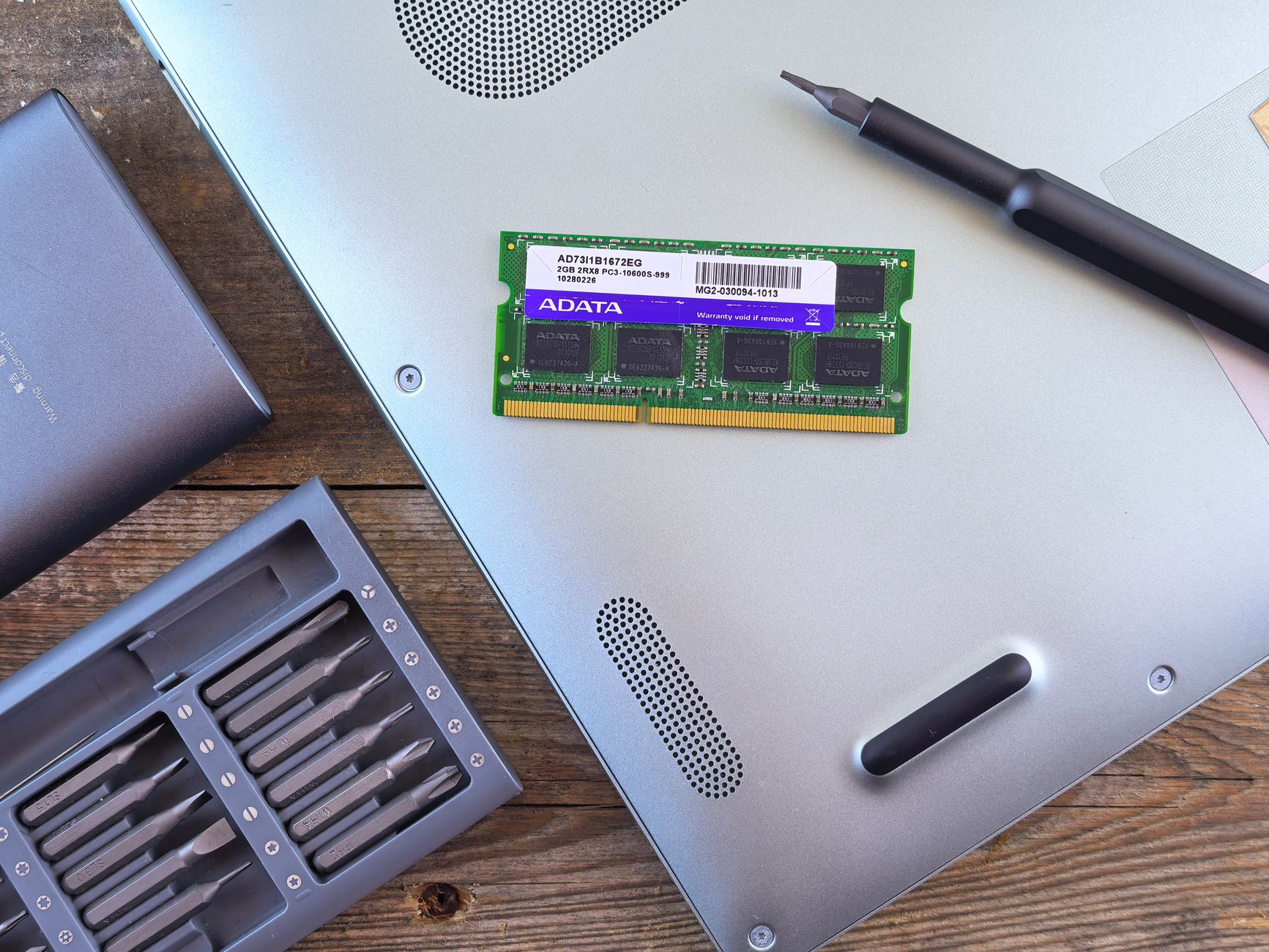 A laptop memory module resting on an open laptop next to a screwdriver set