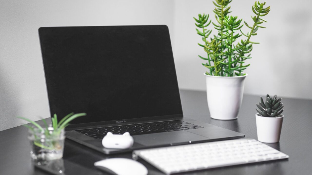 A MacBook Pro on a desk with a keyboard, mouse and plants