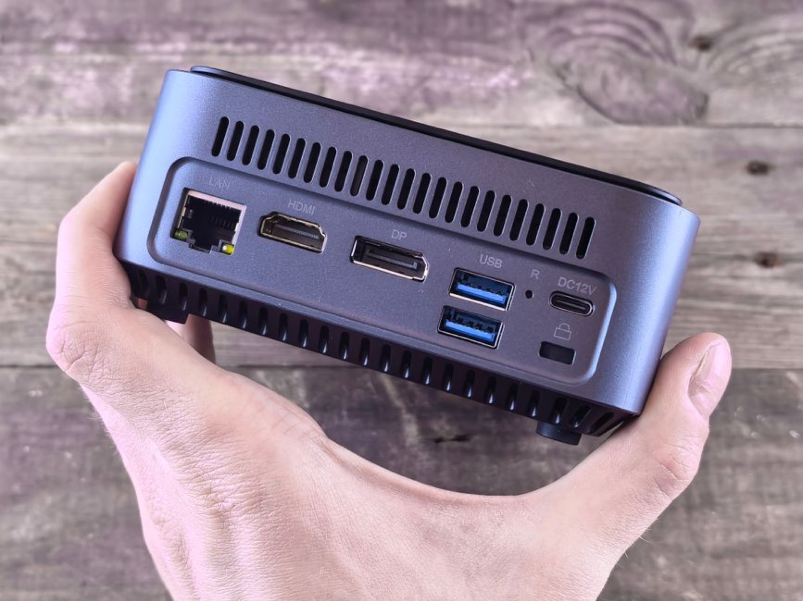 A hand holding a compact mini PC showing its ports