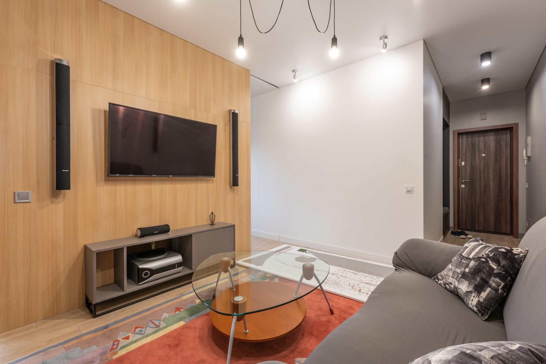 Interior of contemporary light apartment with couch with pillows near table on carpet and cabinet with TV on wall with speakers near lamps on ceiling