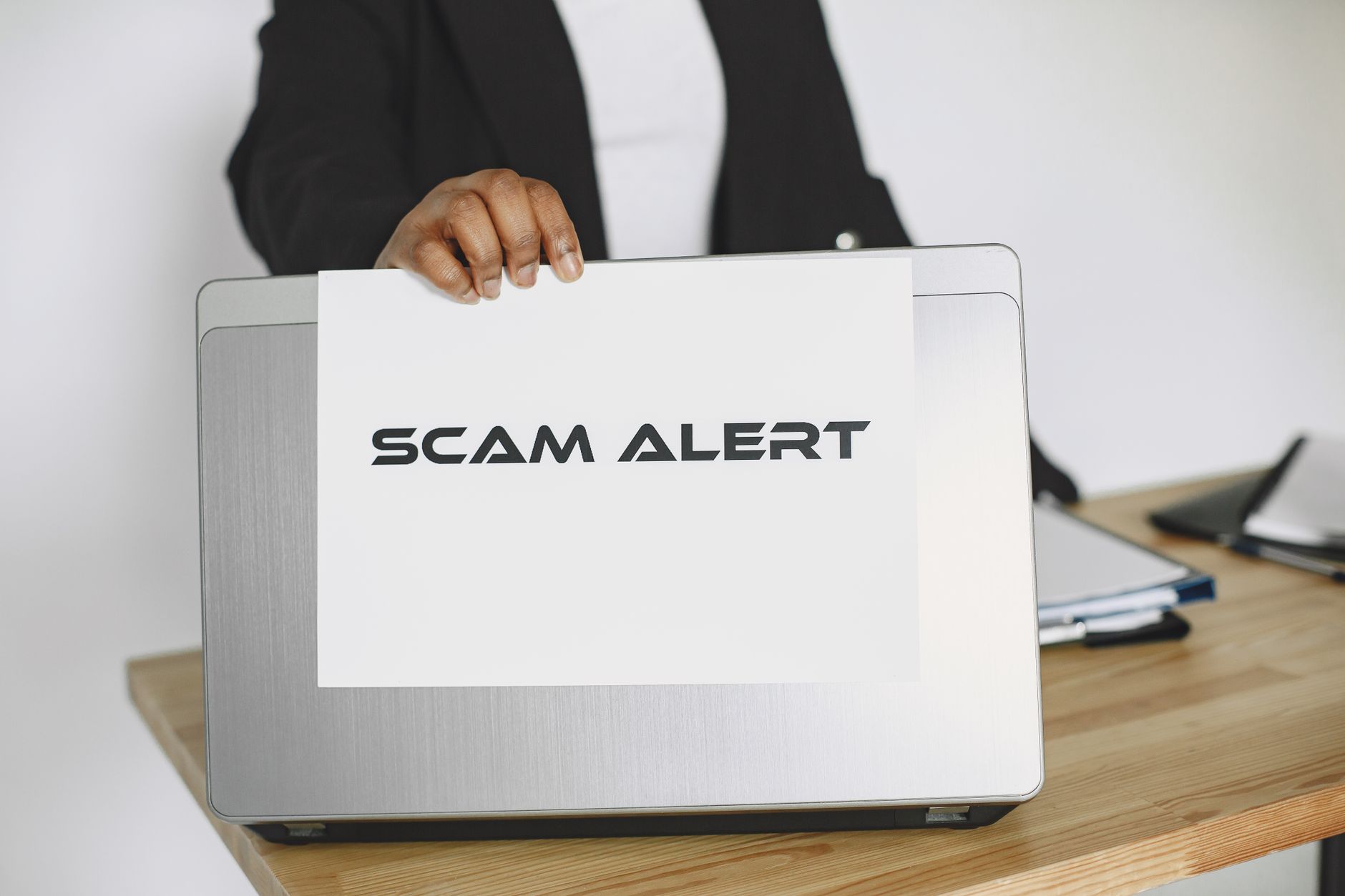 A person holding a scam alert sign over a laptop