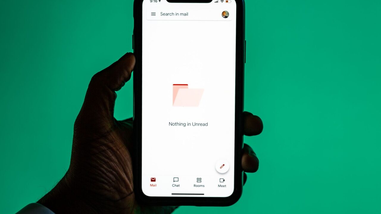 A hand holding a smartphone with an email app open