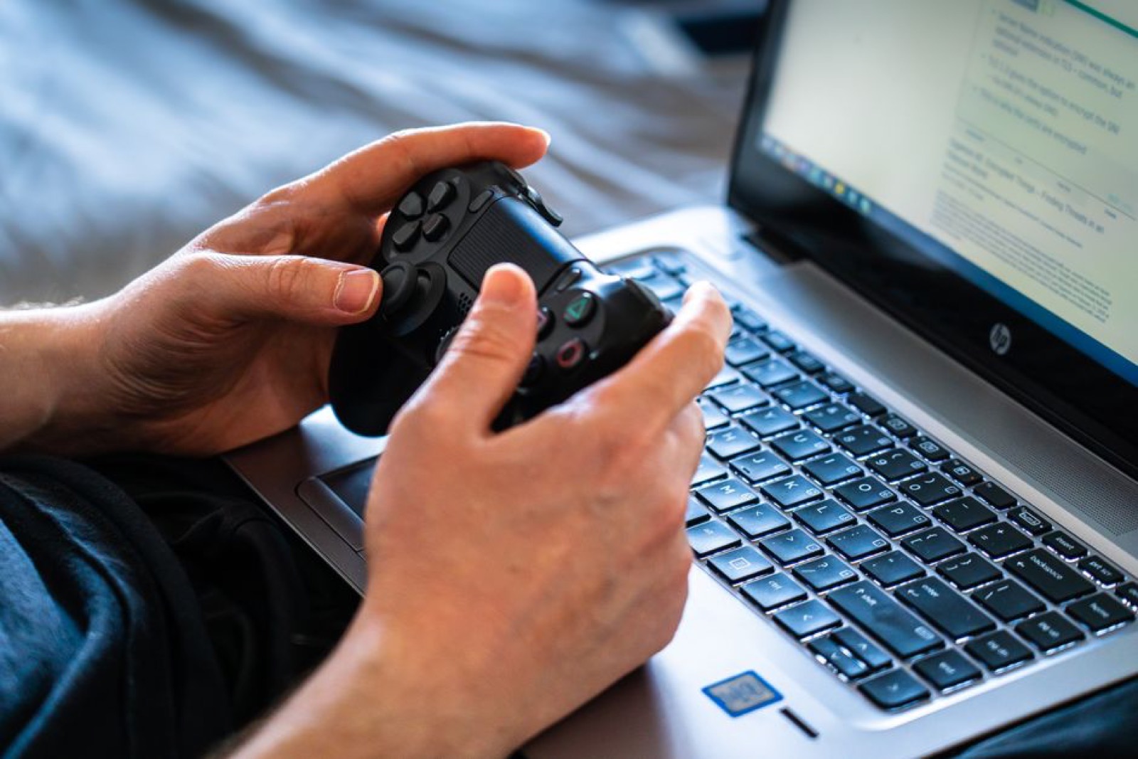A person holding a game controller next to a laptop