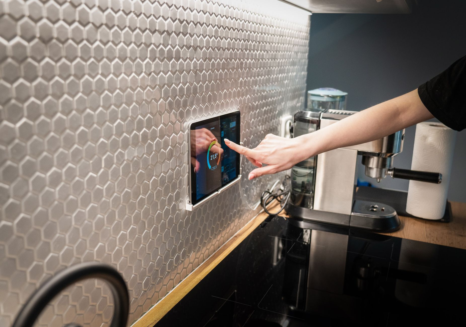 A hand using a wall-mounted smart home control panel in a kitchen