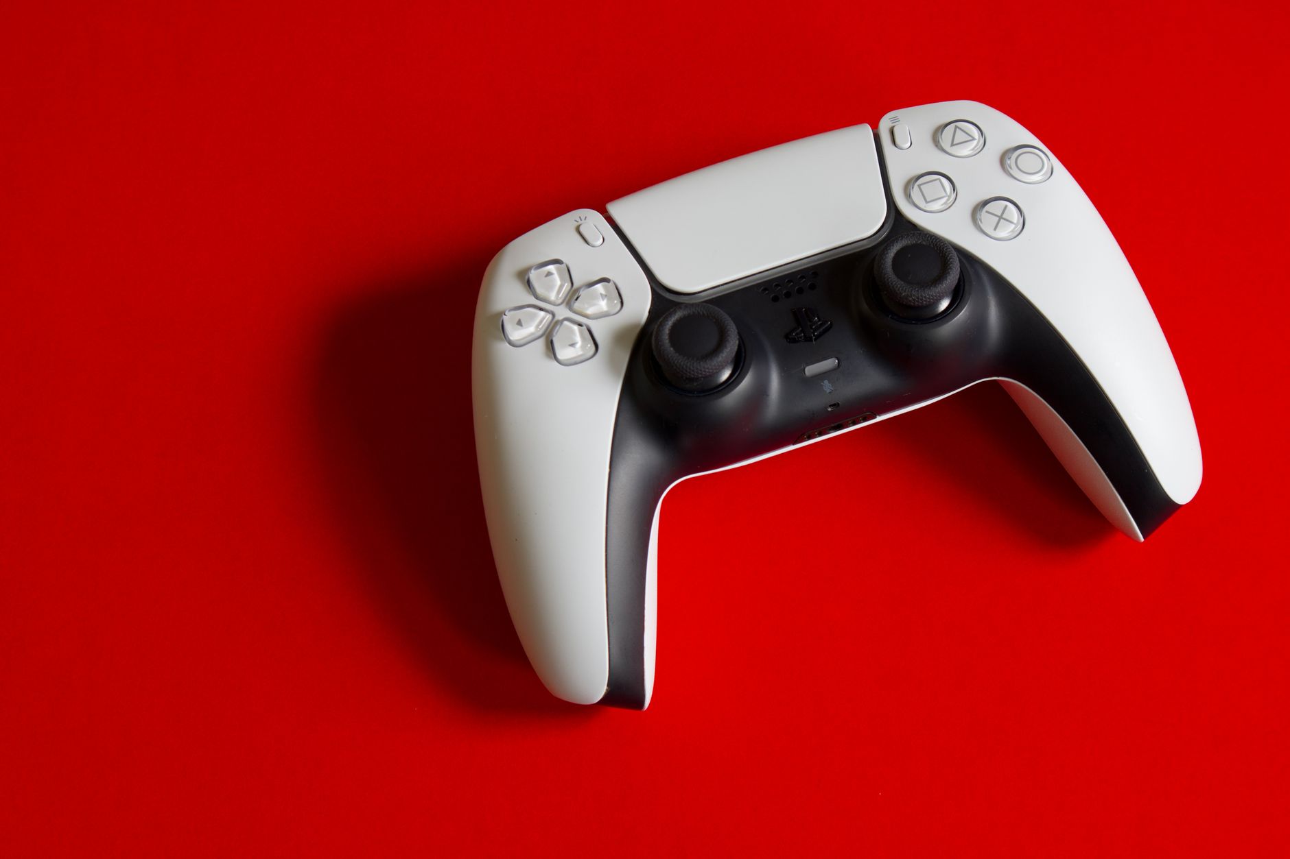 A white PlayStation 5 DualSense controller on a red background