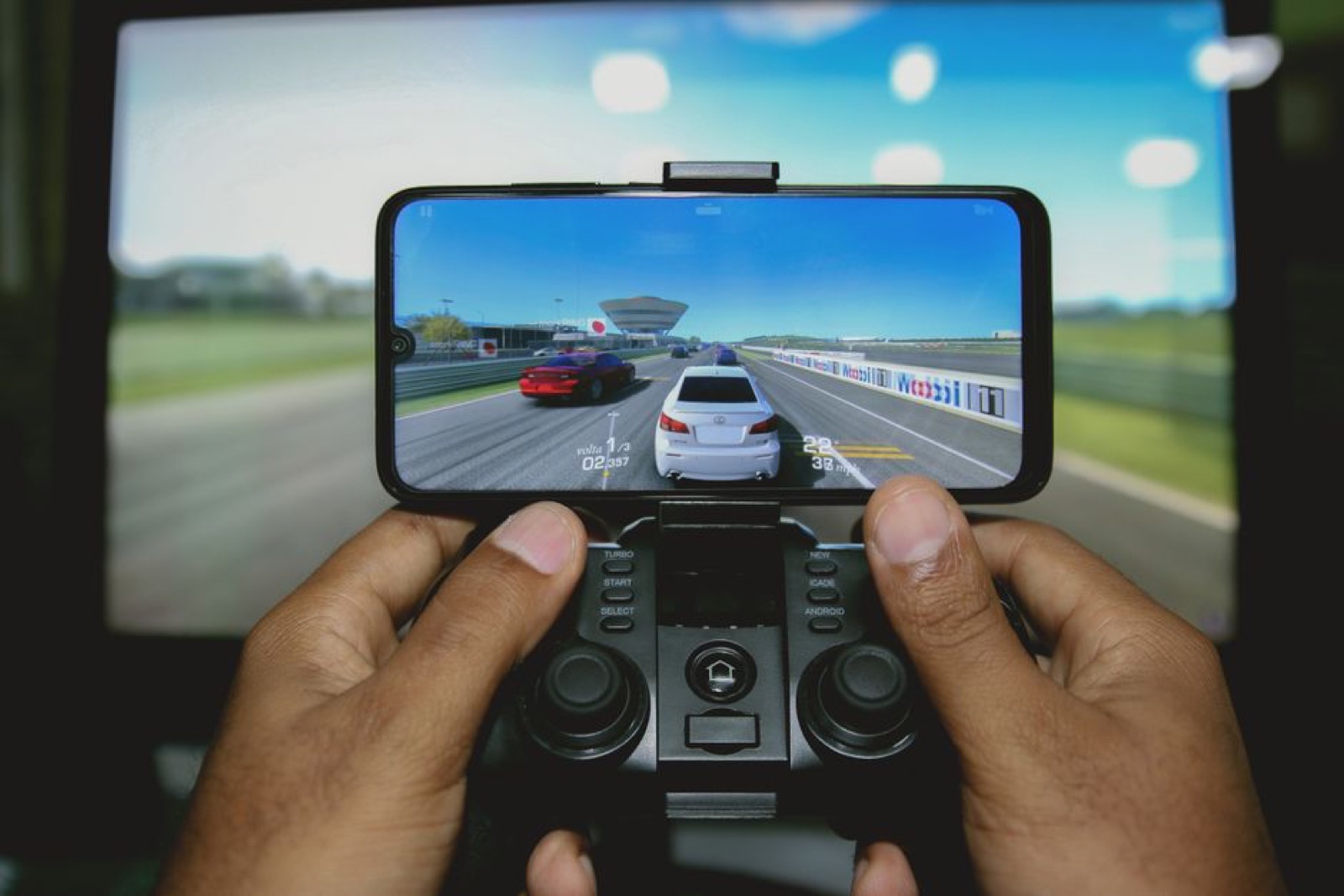 Hands playing a racing game on a phone with a controller